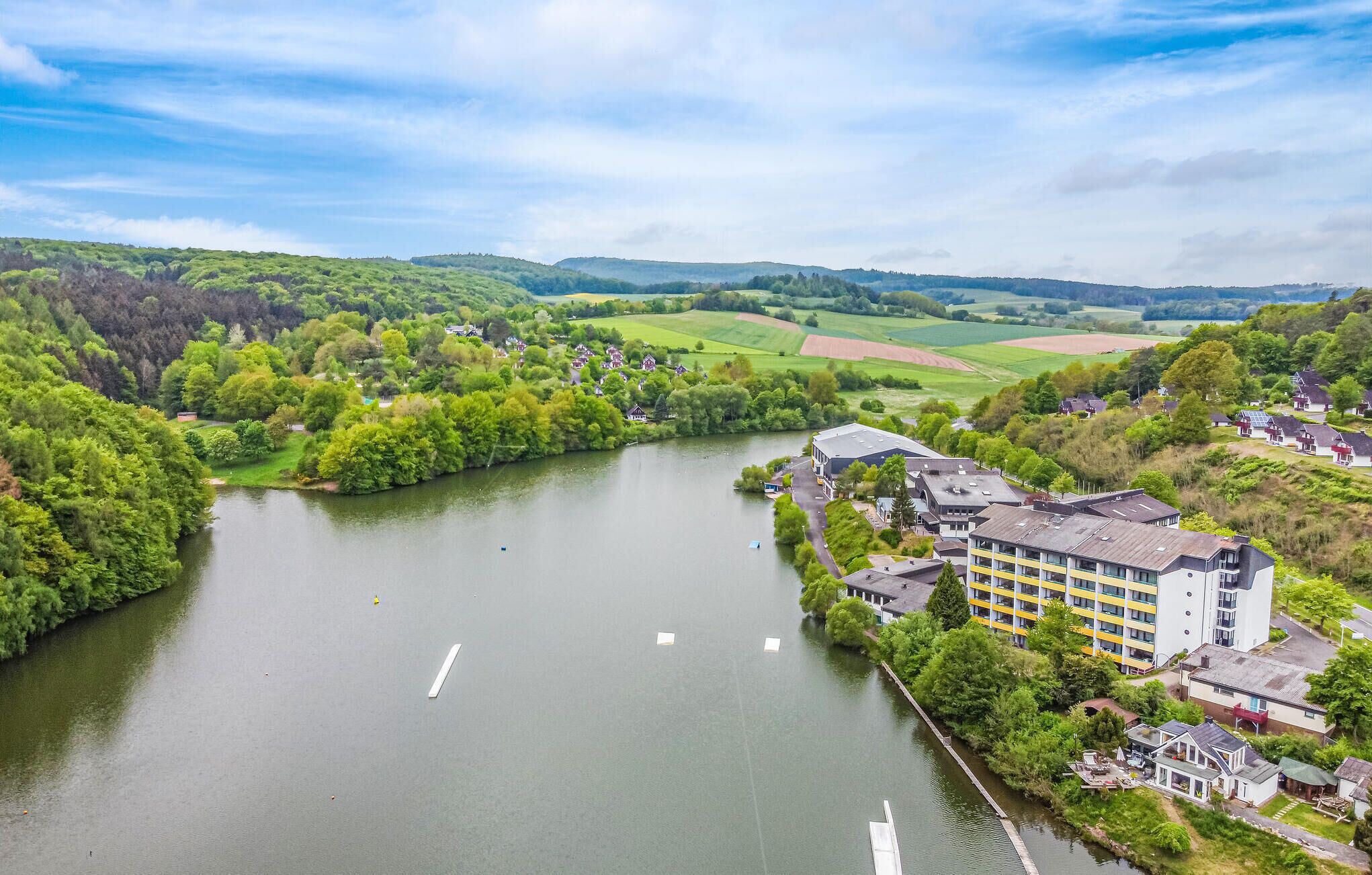 A riverside hotel with a modern building, surrounded by lush greenery and fields.