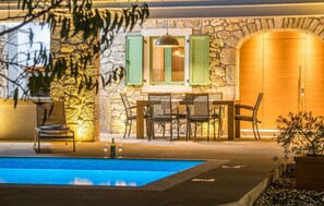 Un área junto a la piscina con un muro de piedra, una puerta de madera y una mesa con sillas.