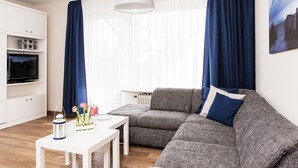 Un salon moderne avec un canapé gris, une table blanche et un téléviseur posé sur un meuble blanc.