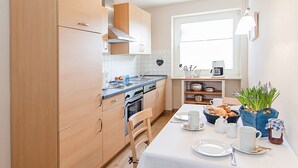 Une cuisine moderne avec des meubles en bois, un four encastré et un coin repas avec une table dressée pour deux personnes.