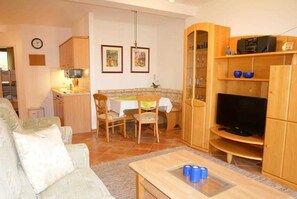 A living room with a sofa, a coffee table, a TV, and a dining area with chairs and a table.
