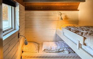 Una habitación pequeña y funcional con una cama litera, una cama individual y una ventana.