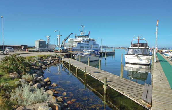 Un port de plaisance avec des bateaux amarrés, une jetée s’avançant dans une eau calme et, au loin, des bâtiments industriels.