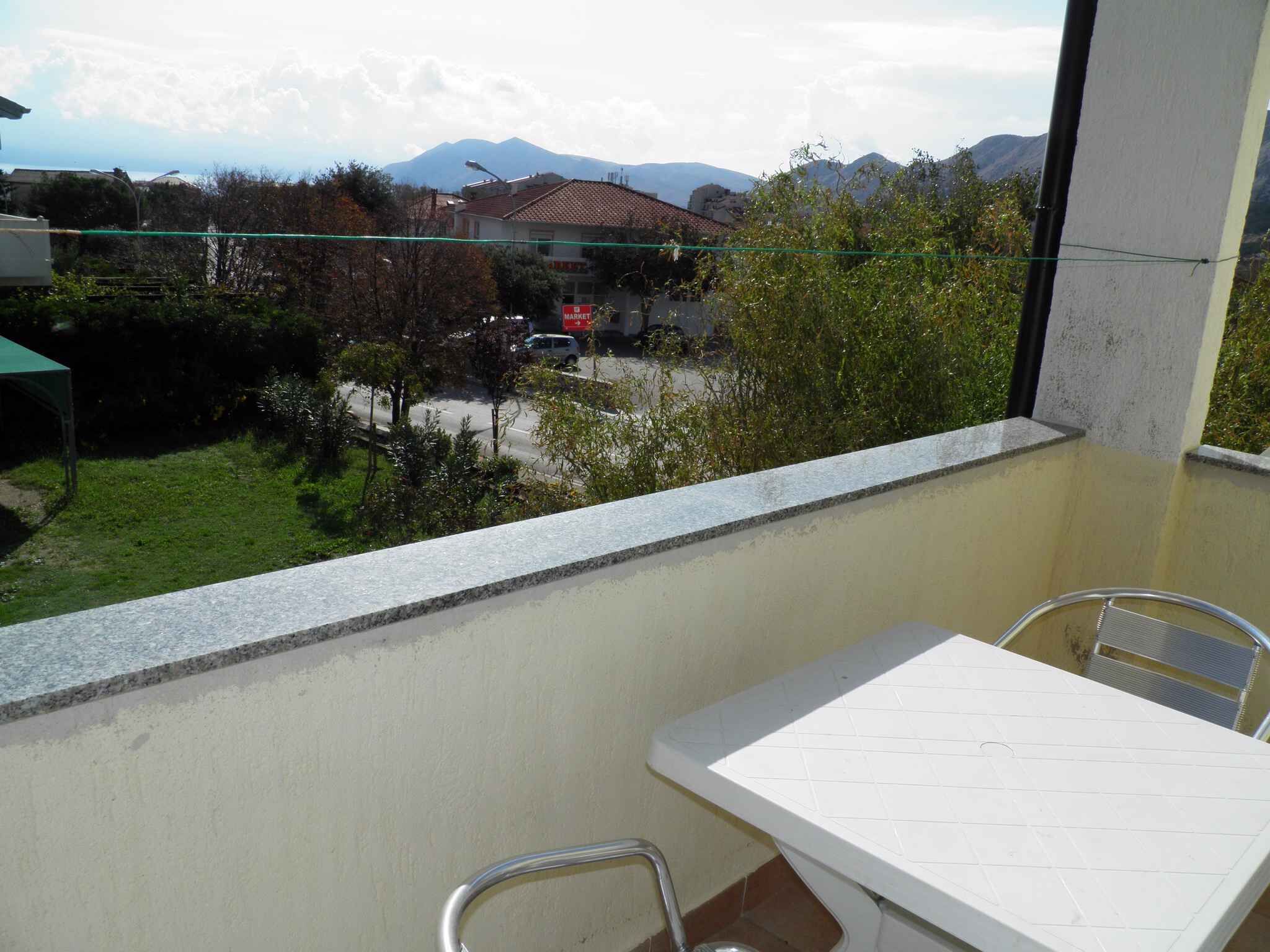 A balcony with a view of a street, a mountain in the background, and a table with chairs.