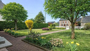 Een verzorgde tuin met een geplaveid pad, bloeiende planten en een stenen gebouw op de achtergrond.