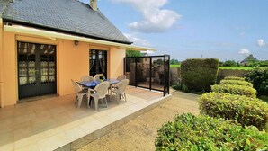 Een huis met een terras, een eettafel met stoelen en een glazen overkapping.