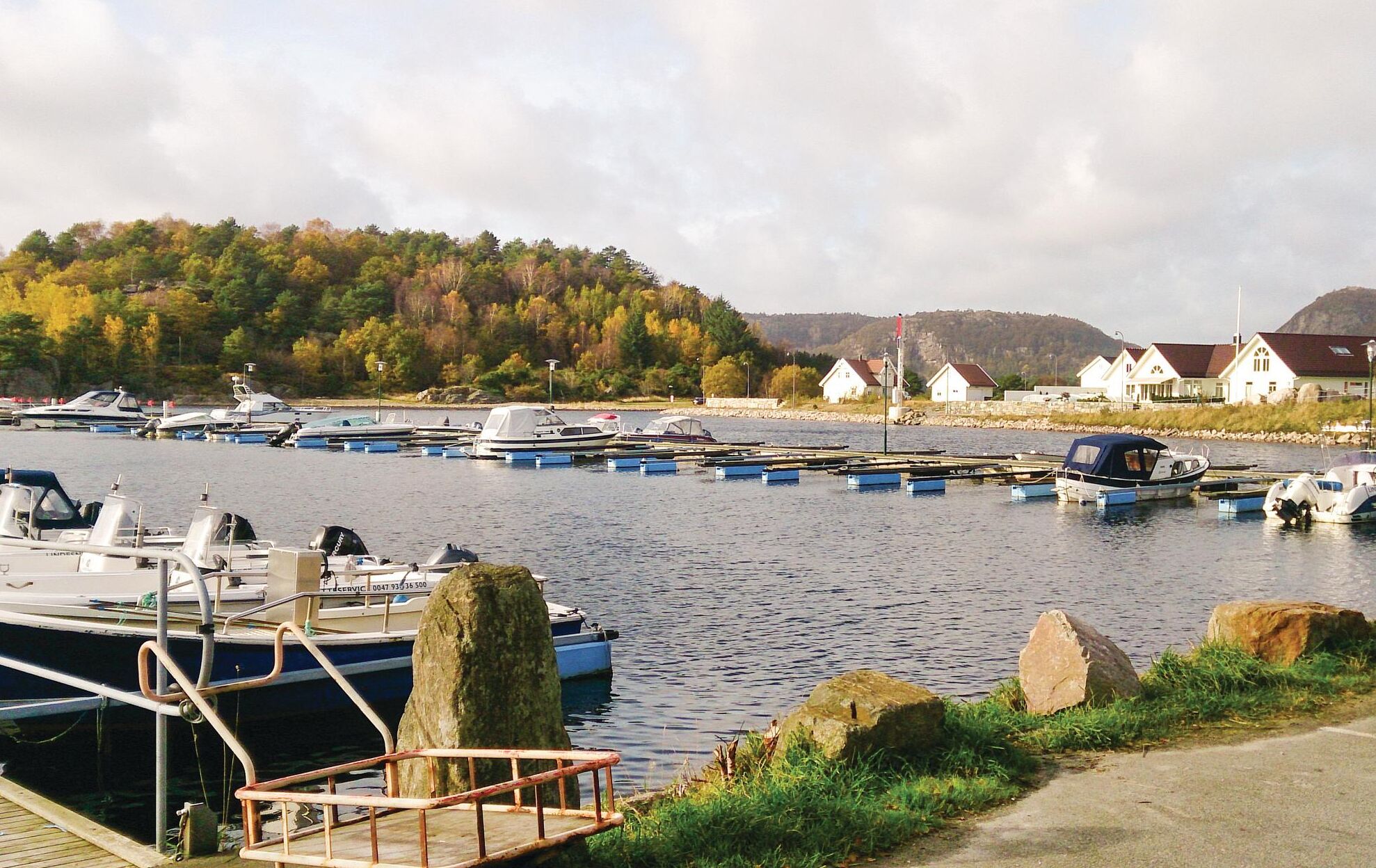 Ein Yachthafen mit vertäuten Booten, eine Holzsteganlage und Häuser im Hintergrund.