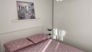 A bedroom with a bed, a wall-mounted picture, a white ceiling light, and a bedside table with a lamp. - Holiday apartment with air conditioning and terrace (Kampor)
