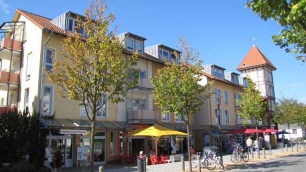 A street with buildings, trees, and a yellow umbrella. - (110) 3-room apartment - lake view - apartment complex Baltic Sea (Kühlungsborn)