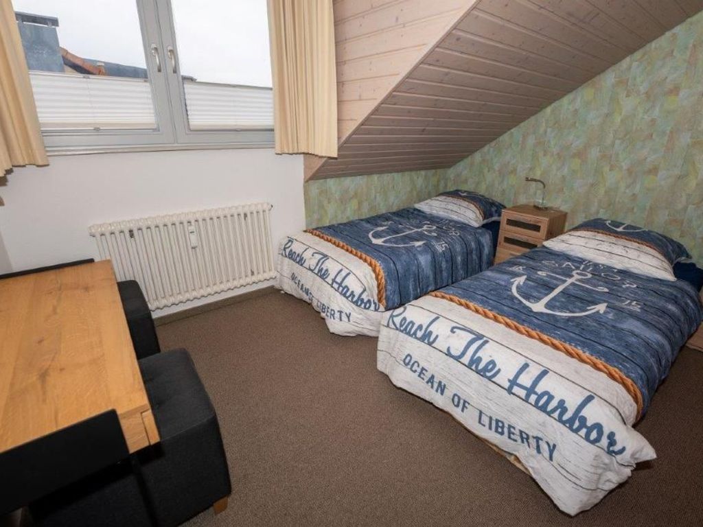 A room with two beds, a wooden table, a radiator, and a window with curtains.