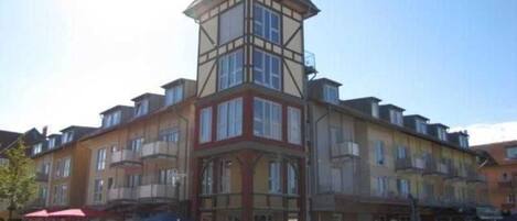 A multi-story building with a prominent corner tower, balconies, and a ground-level entrance.