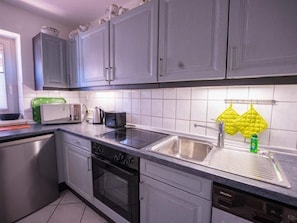 A kitchen with grey cabinets, a microwave, a kettle, a sink, and a dishwasher. - (110) 3-room apartment - lake view - apartment complex Baltic Sea (Kühlungsborn)