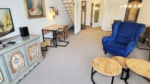 A living room with a blue armchair, a wooden coffee table, a dining table, and a staircase leading to another room. - (110) 3-room apartment - lake view - apartment complex Baltic Sea (Kühlungsborn)