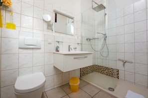 A bathroom with a toilet, sink, mirror, shower, and a glass-enclosed shower stall.