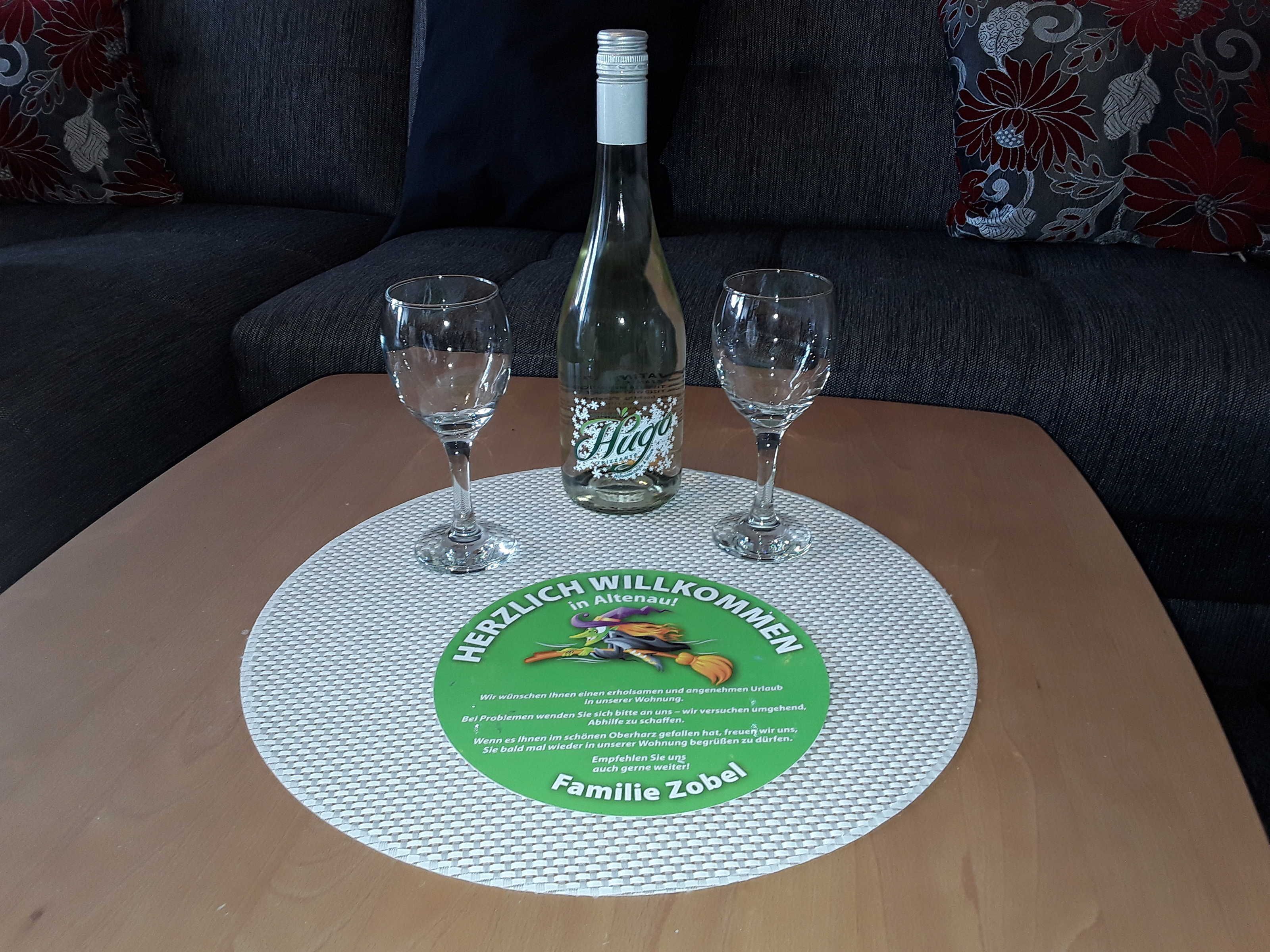 Ett bord med en underlägg som har text på sig, en flaska Hoya-vin, två glas och en soffa i bakgrunden.