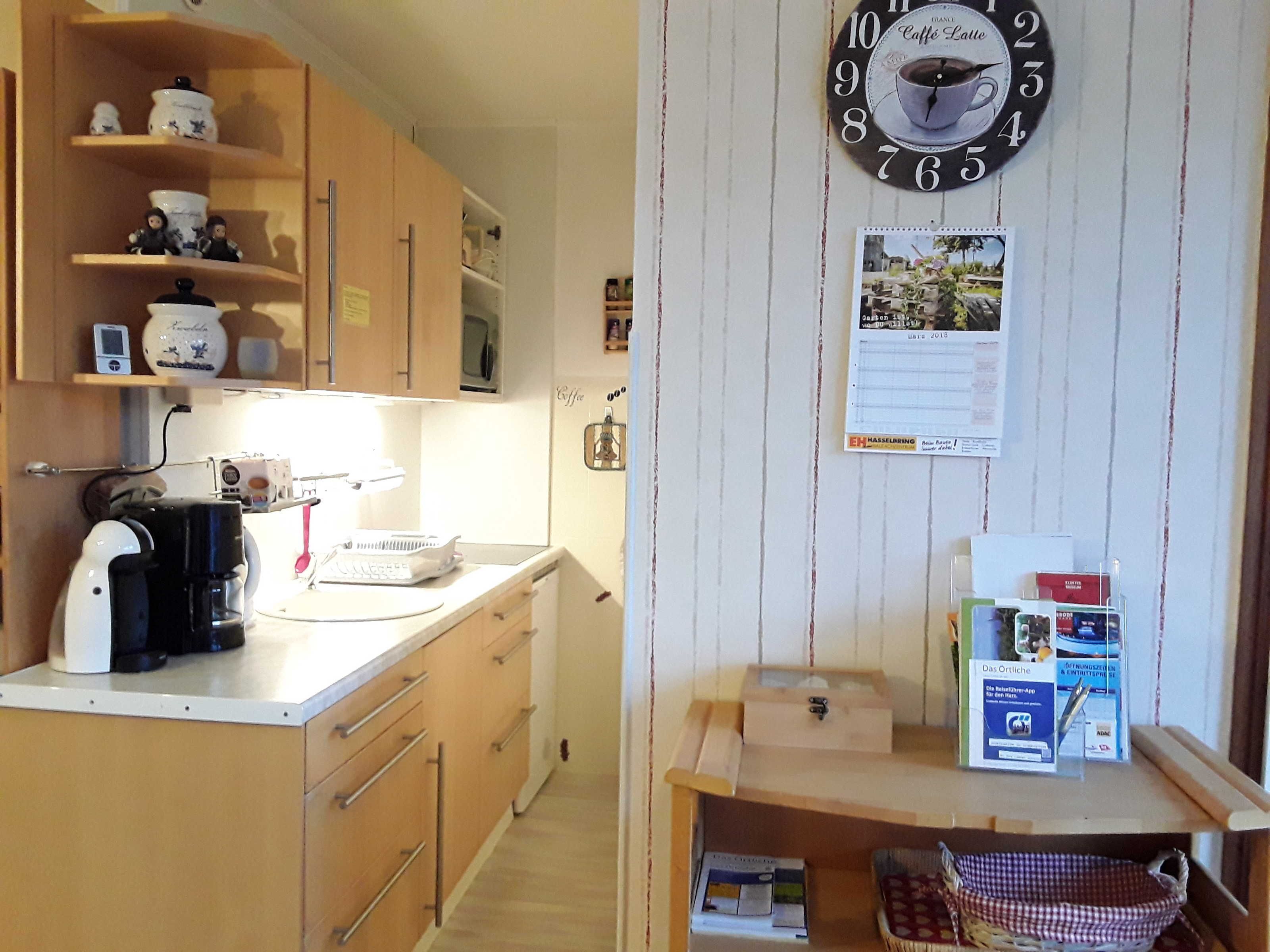 A compact kitchen with wooden cabinets, a coffee machine, and a wall clock.