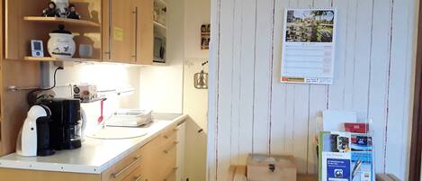 A compact kitchen with wooden cabinets, a coffee machine, and a wall clock.