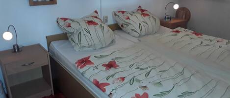 A bedroom with a bed, nightstands, a lamp, and wall-mounted shelves with decorative items.