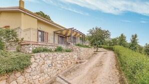 A two-story building with a stone retaining wall, a covered outdoor area with a pergola, and a dirt path leading to a green landscape. - Gorgeous home in Sperlonga -LT- (Sperlonga -LT-)
