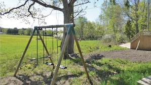 A swing set in a grassy area with a tree and a wooden structure in the background. - 2 bedroom stunning home in Strängnäs (Strängnäs)