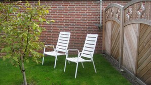 Eine Terrasse mit zwei weißen Metallstühlen und einem kleinen Baum.