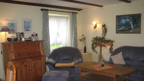 Ein Wohnzimmer mit Holzschrank, blauem Sessel, passendem Hocker und Couchtisch.