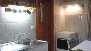 Eine Küche mit Spüle aus Edelstahl, weißen Schränken, einem weißen Herd und einer Holztür.