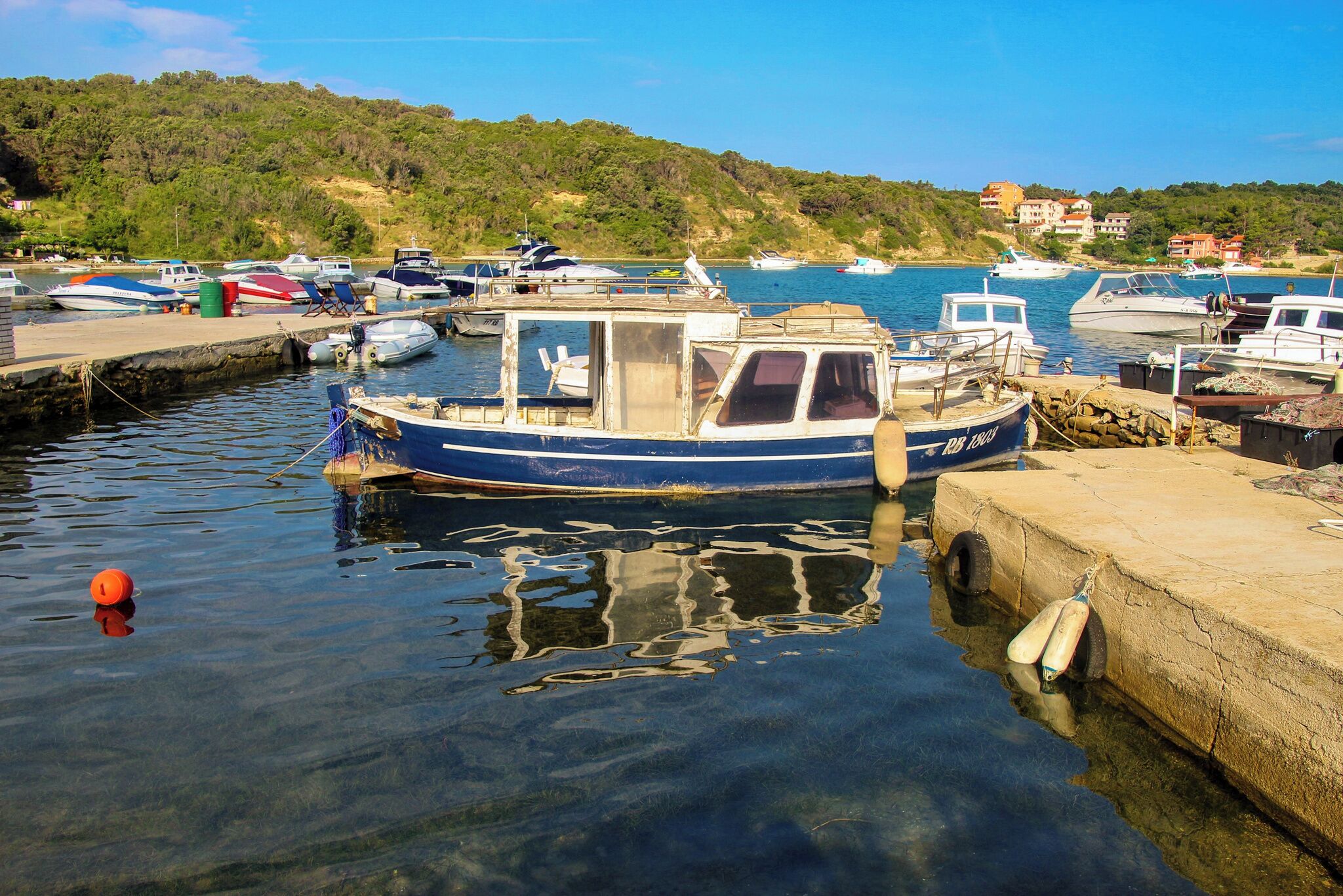 Un puerto deportivo con barcos amarrados, cielo despejado y un paisaje montañoso al fondo.