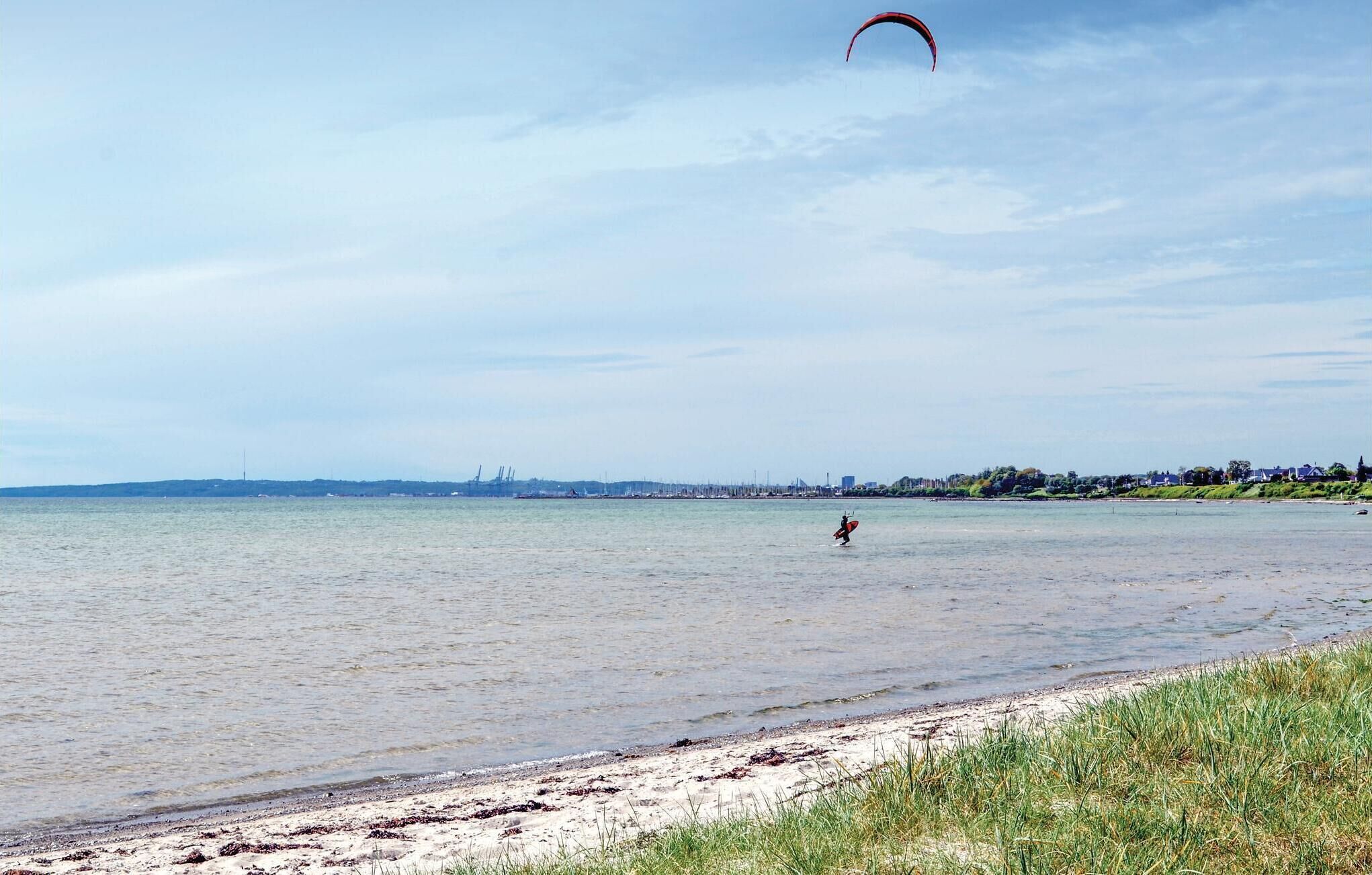 Een strand met een persoon die windsurft, een verre kustlijn met gebouwen, en een heldere lucht.