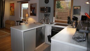 Une cuisine compacte équipée d’un lave-vaisselle, d’un four et d’un four à micro-ondes. Une fenêtre laisse entrer la lumière naturelle et offre une vue sur l’extérieur.