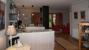 Une cuisine moderne dotée d’un îlot central, un coin repas avec une table et des chaises, et un salon avec un canapé rouge et une table basse.