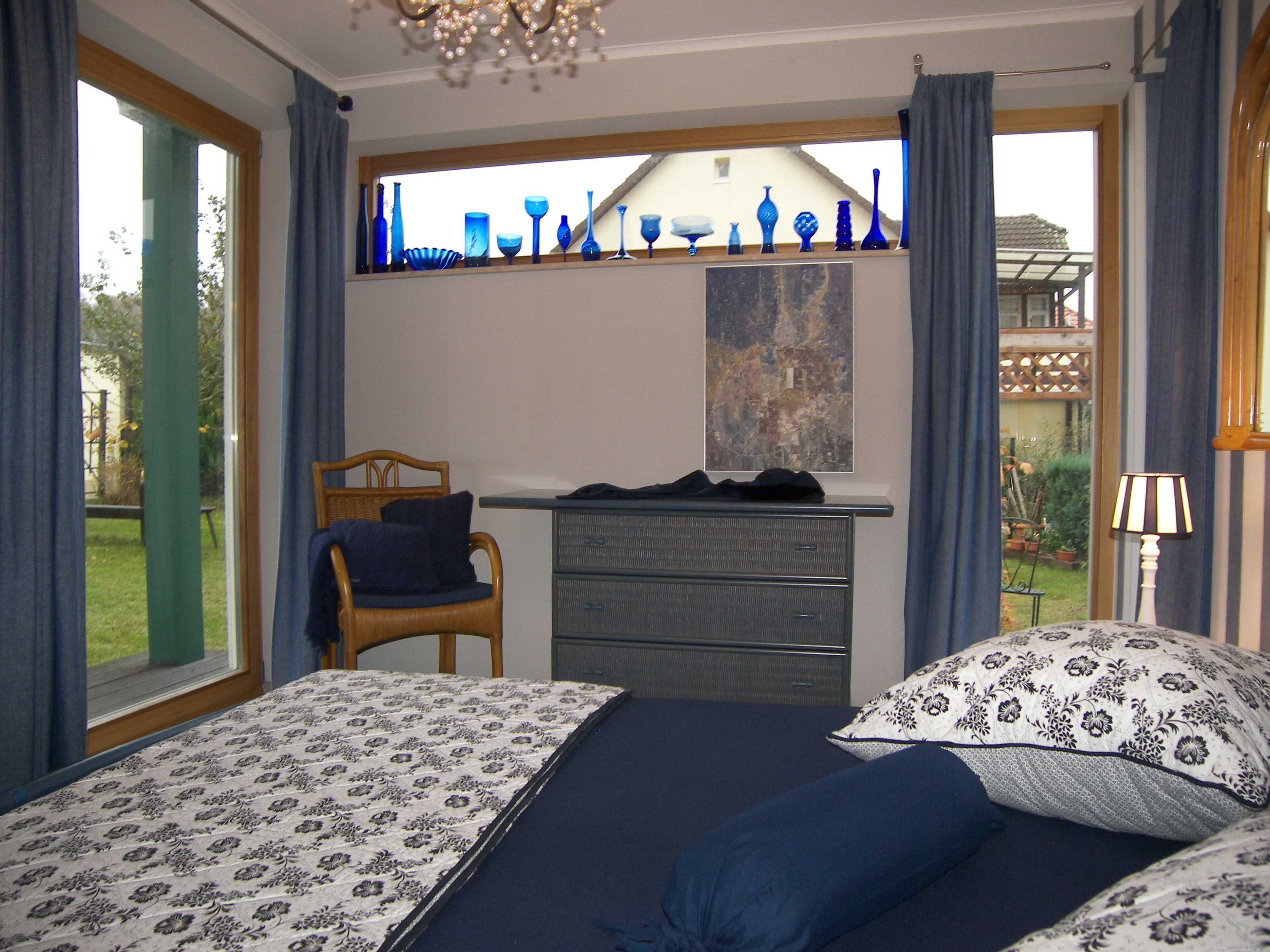 Een slaapkamer met twee bedden, een dressoir, een stoel, een raam met blauw glaswerk en uitzicht op de omgeving.
