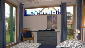 Une chambre avec deux lits, une commode, une chaise, une fenêtre ornée de vitraux bleus et une vue sur l’extérieur.