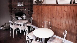 A cozy dining area with a brick fireplace, white metal chairs, and a round table. - Ferienzimmer Moorhexe - Holiday room in Graal-Müritz (Graal-Müritz)