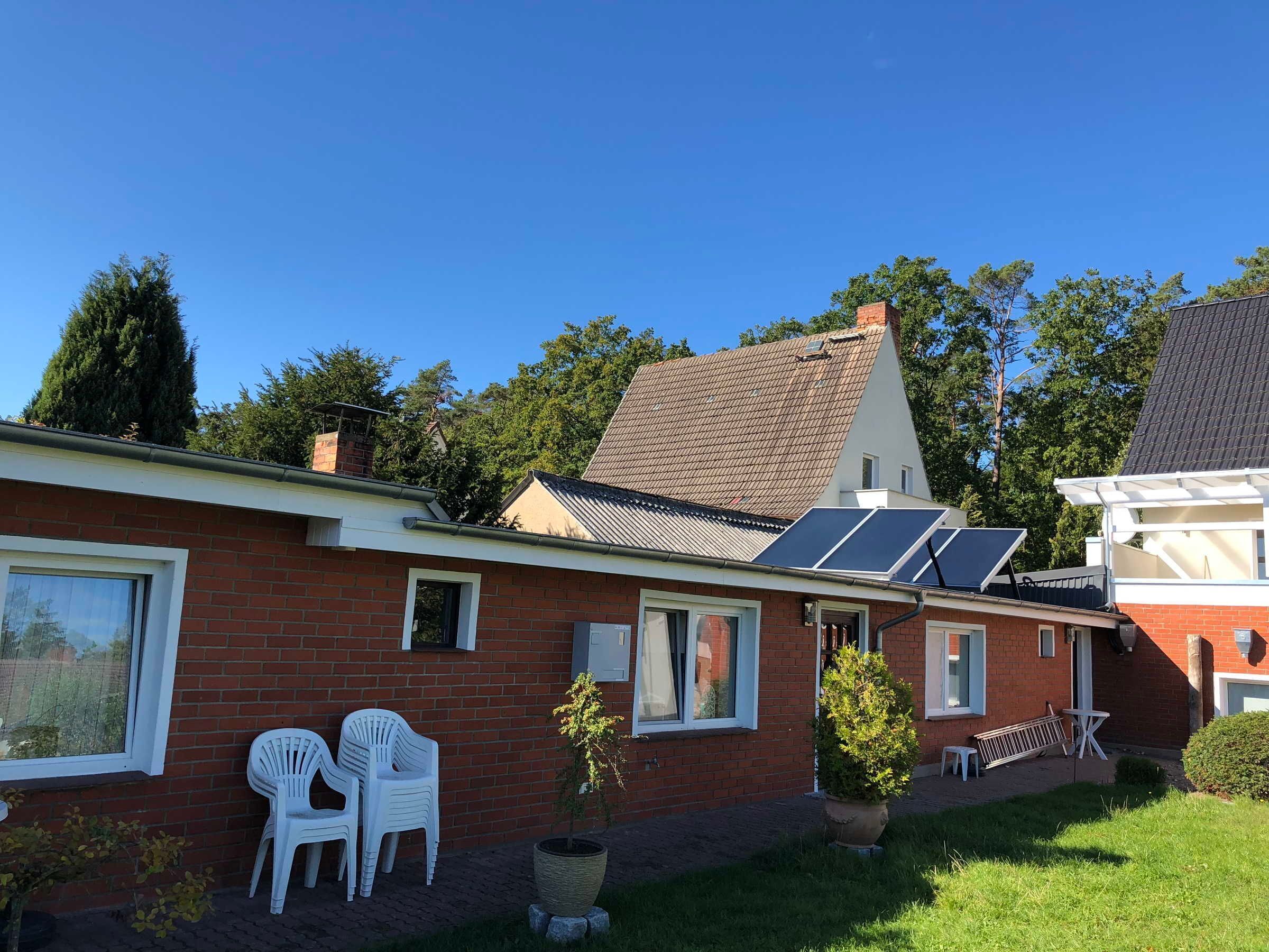 A brick house with solar panels, white plastic chairs, and a potted plant.