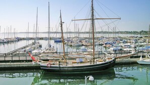 Un porto turistico con diverse imbarcazioni ormeggiate, una barca a vela in primo piano e acque calme che riflettono le imbarcazioni.