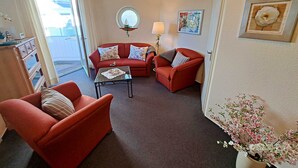 Una sala de estar con un sofá rojo, un sillón rojo más pequeño, una mesa de centro de vidrio y una planta en maceta.