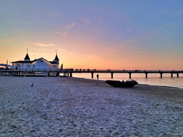 A beach with a pier, a boat, and a building with two towers.