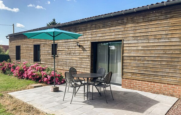 Un patio con mesa y sillas, un parasol verde y un edificio de ladrillo con revestimiento de madera.