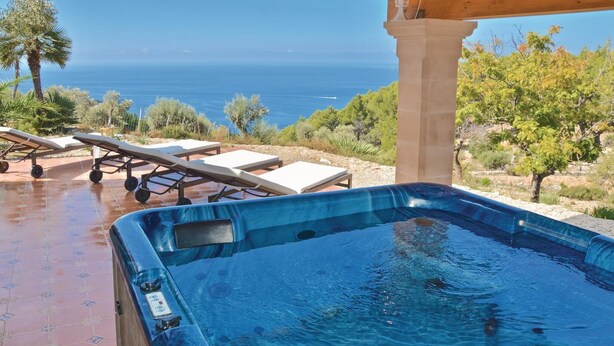 A hot tub with a clear view of the sea, lounge chairs, and a pergola structure.