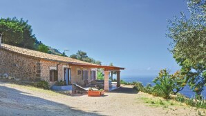 A stone house with a tiled roof, a covered patio, and a view of the sea.