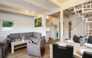 A modern living room with a grey sectional sofa, a small coffee table, and a dining area with a wooden table set for a meal. - Lovely home in Thale with sauna (Thale)