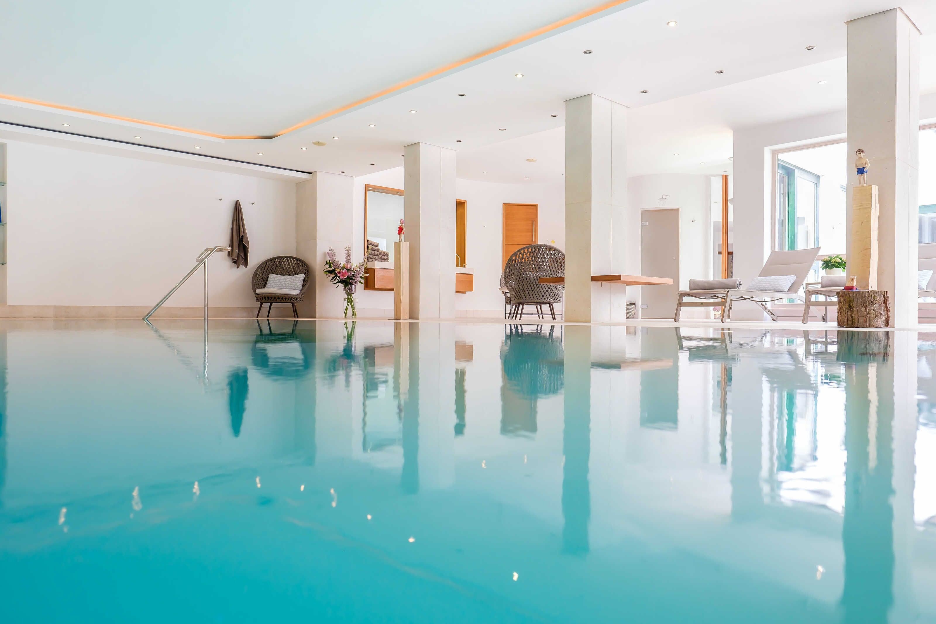 Une vaste piscine intérieure à l’eau claire, entourée de chaises longues modernes et dotée d’un intérieur épuré et minimaliste.