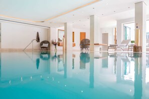 Una amplia piscina interior con agua cristalina, rodeada de modernas sillas de descanso y un interior limpio y minimalista.