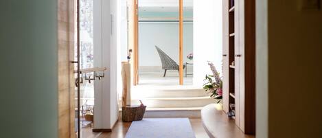 A hallway with a wooden floor, a blue rug, a chair, and a staircase leading to a balcony.