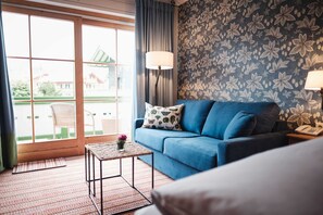 A room with a blue sofa, a small table with a lamp, a patterned wall, and a view through a window.