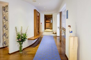 A hallway with a blue patterned carpet, wooden shelves, a vase with flowers, and a wooden sculpture. - Single Room - Landhaus am Stein (Bad Wiessee)