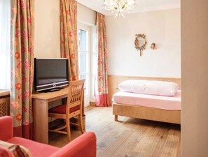 A bedroom with a bed, a desk with a television, a chair, and floral curtains.