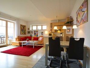 Ein modernes Wohnzimmer mit rotem Teppich, einem beigefarbenen Sofa und einem Essbereich mit zwei Stühlen.