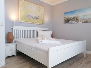 Ein Schlafzimmer mit einem weißen Bett, einem Nachttisch, einer Lampe und zwei Bildern an der Wand.
